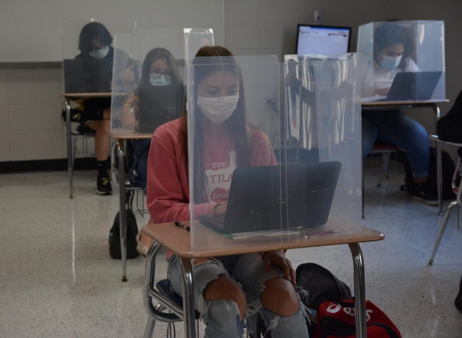 Navigating her laptop in Geometry class, Kylie Madura, freshman, completes her school work. Classes have taken on a new look this school year, with plastic dividers, masks and new furniture in general.