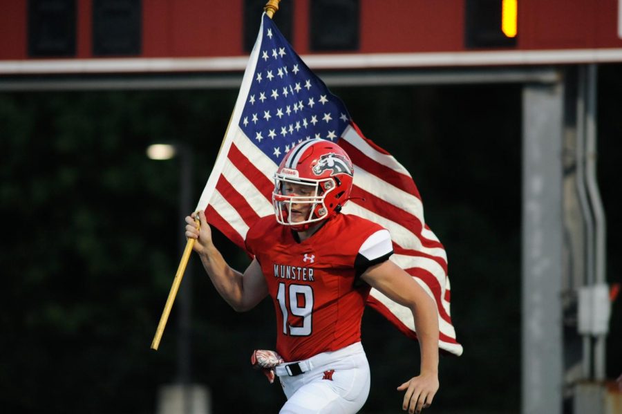 RAISING THE FLAG As the crowd roars, Thomas Choros, senior, carries the American flag in front of the team. Football was ecstatic to play at home against Hanover Central on Aug. 27. “The boys were all buzzing and were ready to hit,” Choros said. “Personally, I was ready to run through a wall.”