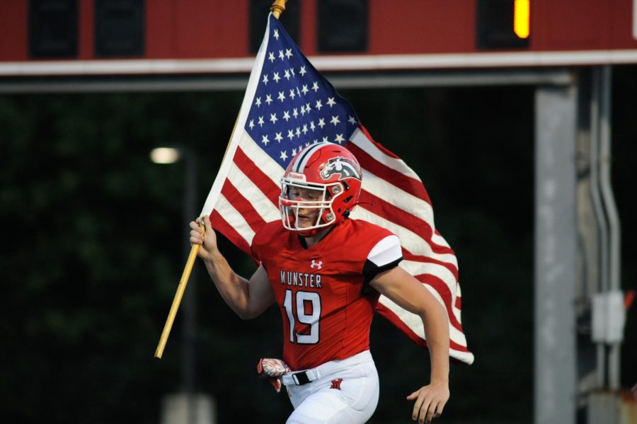 RACE TO THE END ZONE Charging with the flag, Thomas Choros, senior, runs across the football field. The team was pumped for the Aug. 27 game against Hanover Central. “I couldn’t have asked for a better group of guys to play the greatest game on earth with,” Thomas Choros, senior, said.
