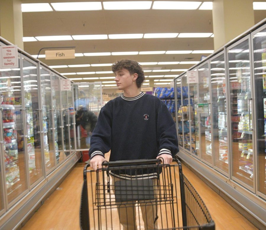 DOWN THE AISLE Posing for a photo in Jewel-Osco, Sonny Hoekstra, senior, reflects on his personal struggle with food insecurity. When he was younger, his family would only buy food in bulk: he recalls having to buy lots of raw ingredients to make everything from scratch. The photo simulates how overwhelming shopping can be. 
