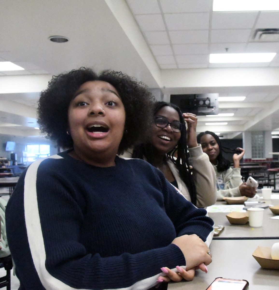 CULTURE COLLAB Sitting in the cafeteria during the Feb. 8 Culture Cuisine Club and BCC collaboration meeting, seniors Kam Hubbard, Nneka Oniah and Niah Maduakolam, junior, watch the presentation about Jamaican culture. “We really just want to have fun with both our members and our community, because a lot of our members’ families are also heavily involved,” Kam said. 